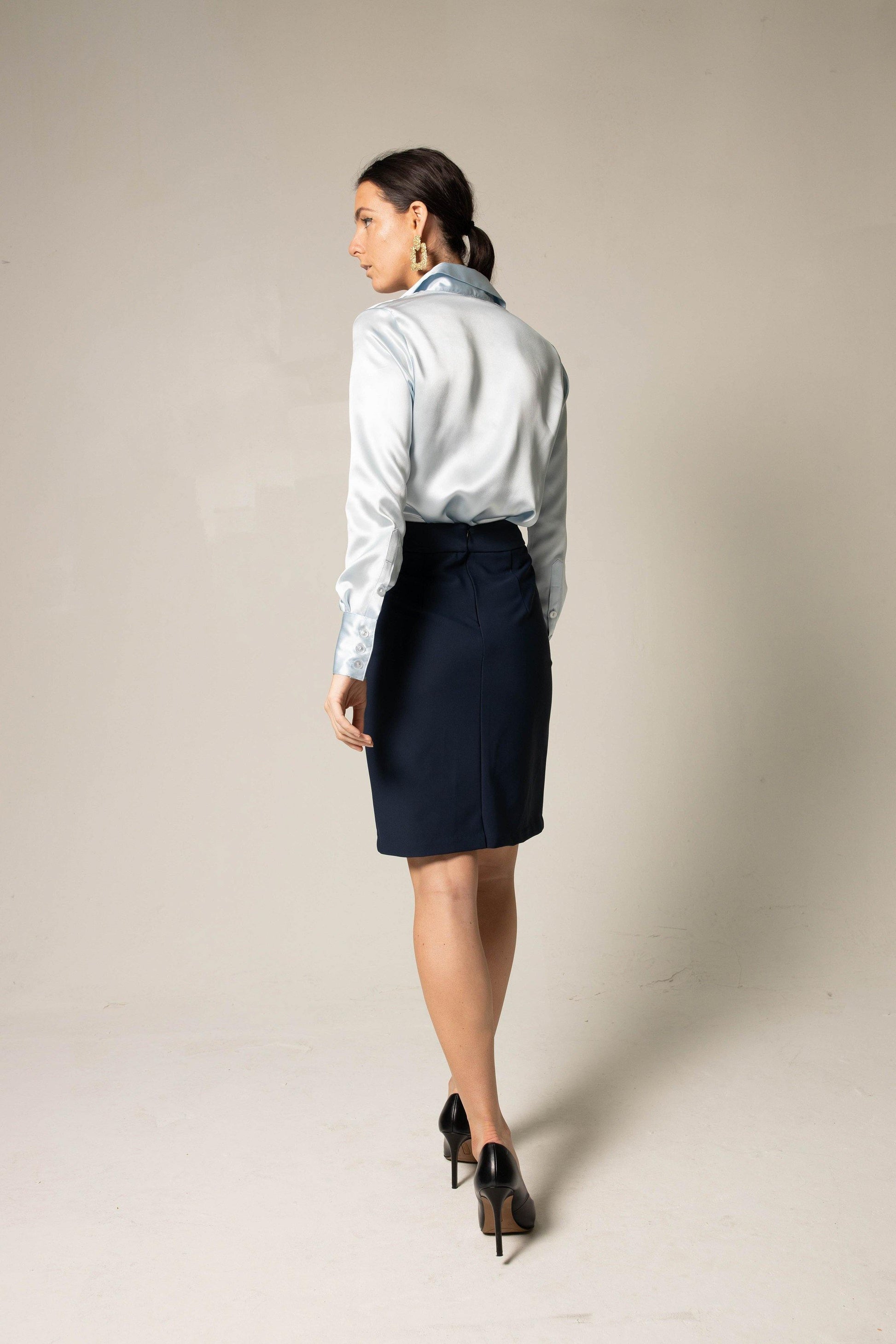 A woman wearing the Classy Silk Shirt in Blue by Le Réussi® stands with hands on hips against a plain background, paired with a dark skirt and gold earrings.