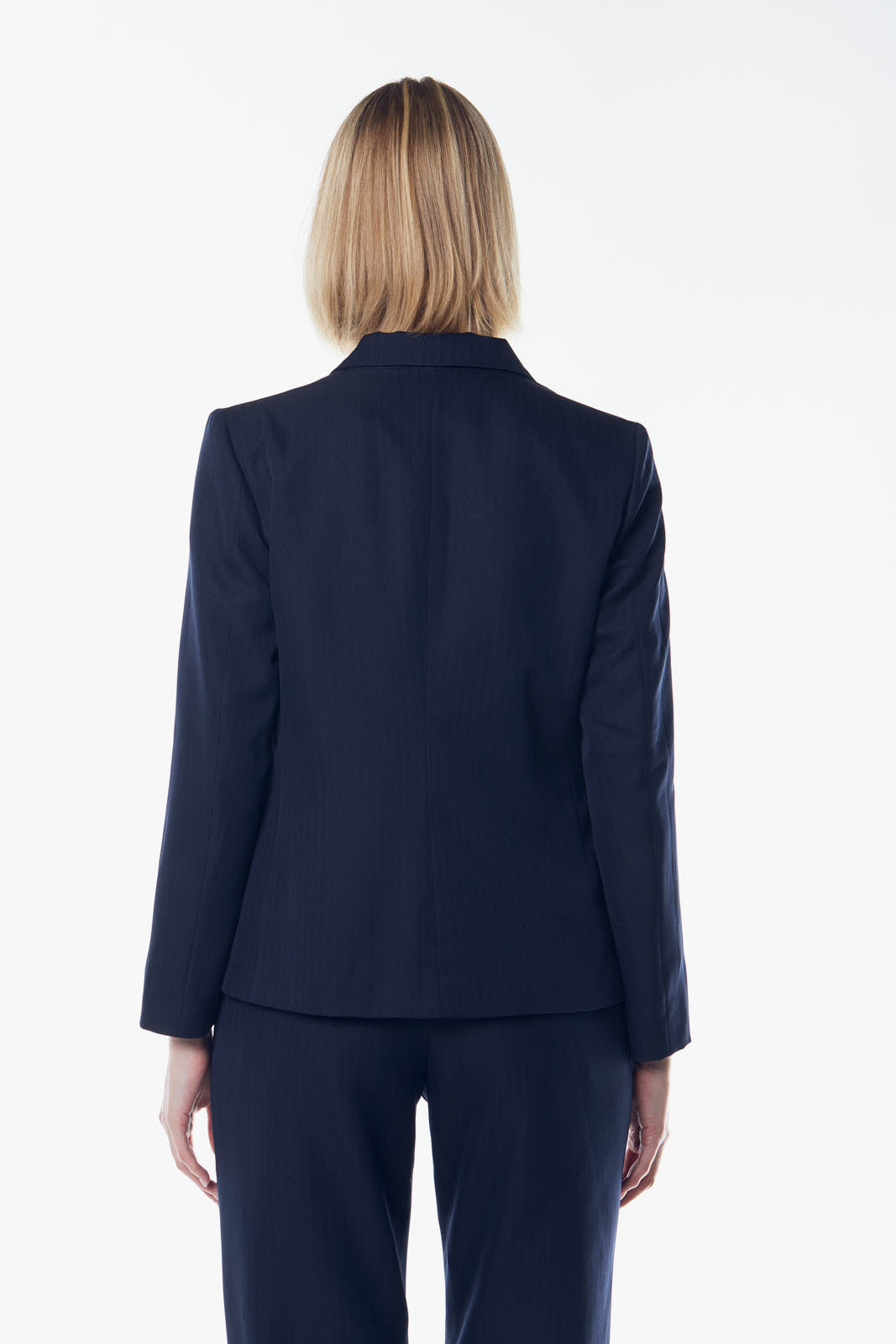 A person in a suit, wearing the Le Réussi® Navy Peak-Lapels Single-Breasted Blazer, stands smiling with one hand on their forehead against a plain background.