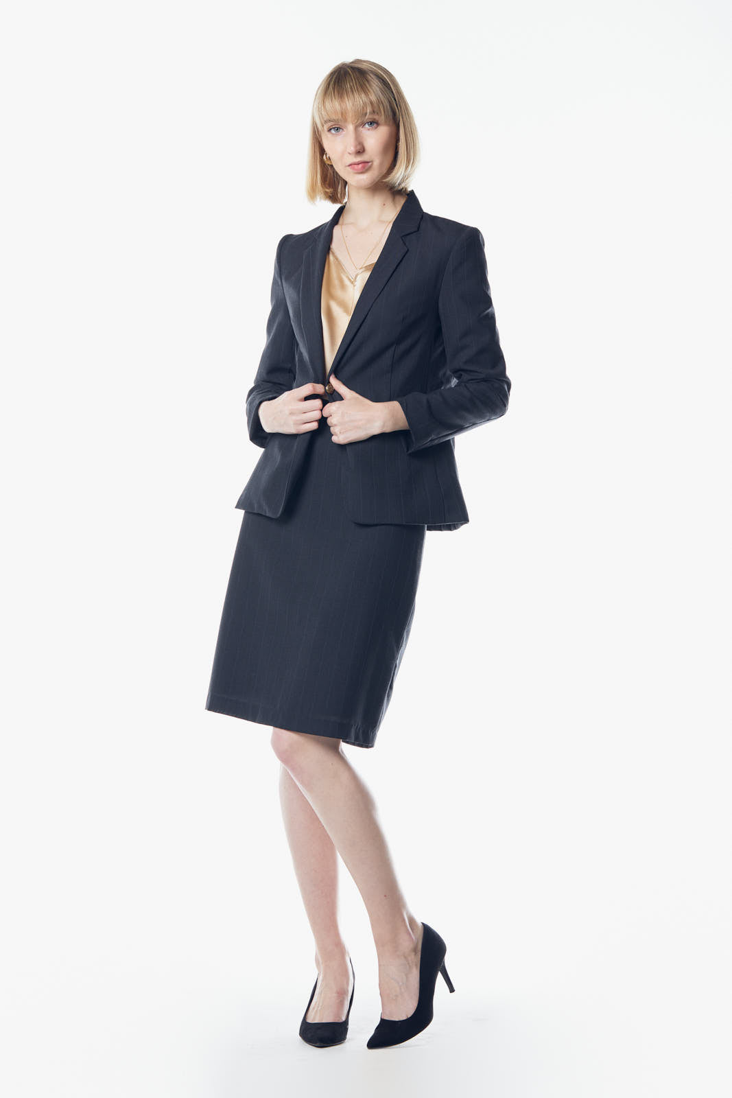 Wearing a Wool Dark Grey Blazer by Le Réussi®, a person with shoulder-length hair holds the edges of their suit, complemented by a beige blouse.