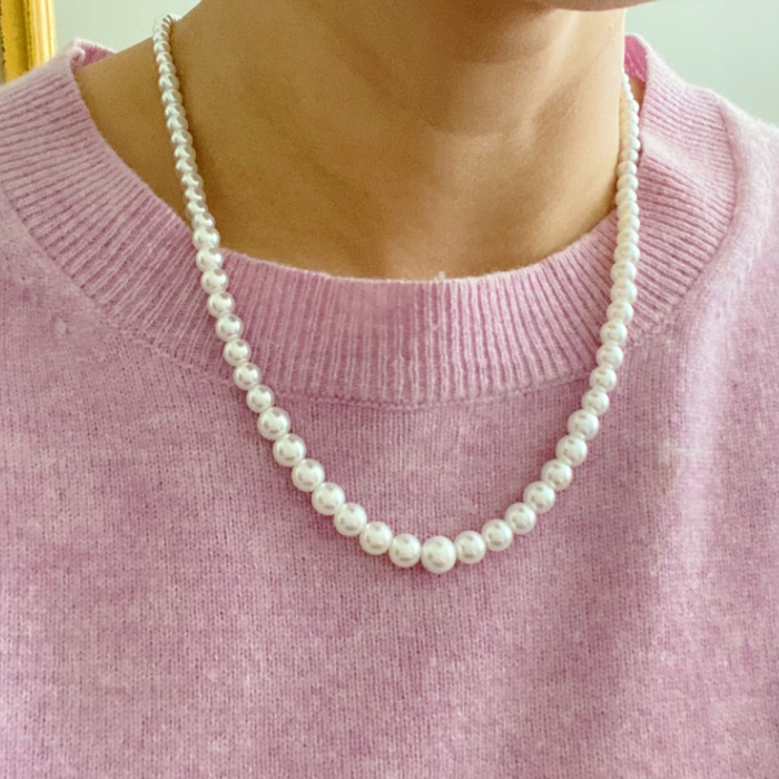 The Queen Liz Graduated Pearl Necklace by Ellison + Young features white pearls with a gold clasp, displayed on a light marble surface.