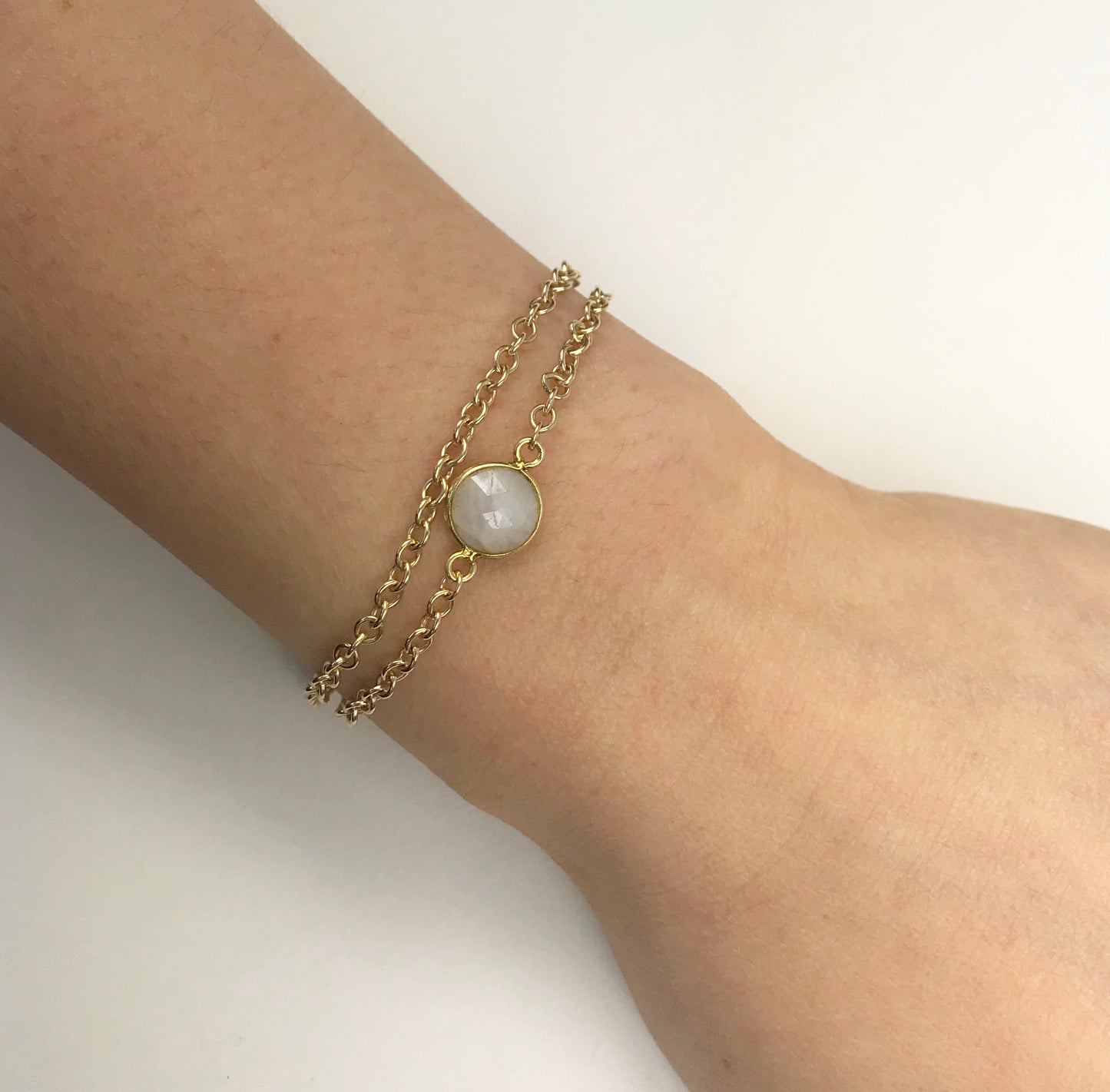 The Gena Myint Moonstone Vermeil Double Chain Bracelet includes a gold double chain design, with a circular white moonstone and a heart-shaped charm on the extender.