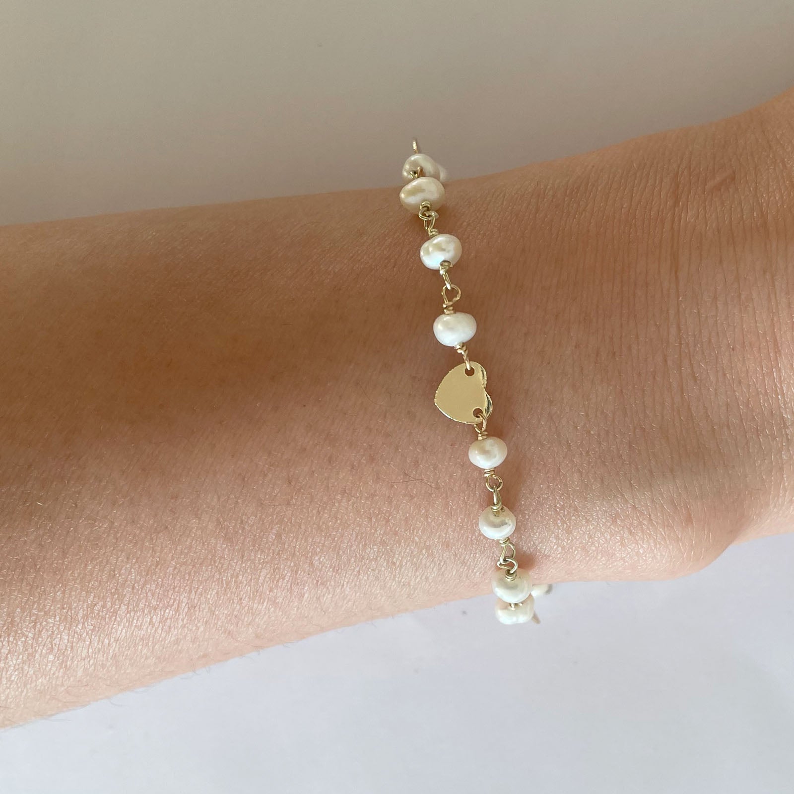 Gena Myints Pearl and Heart Charm Bracelet: A gold bracelet featuring pearl beads and three heart-shaped charms.