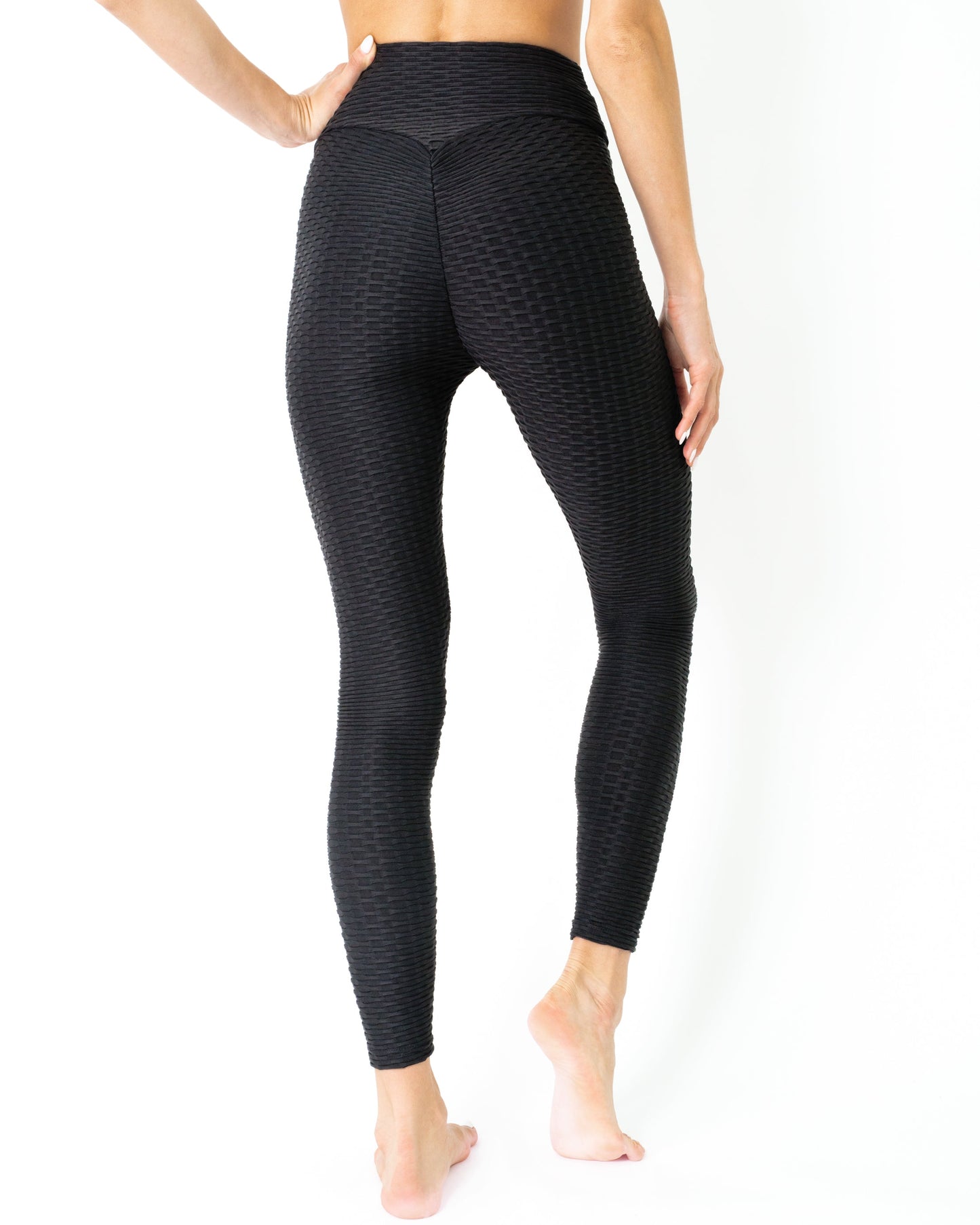 A person in Savoy Actives Bentley Leggings - Black stretches outdoors on a tree-lined paved path with benches.