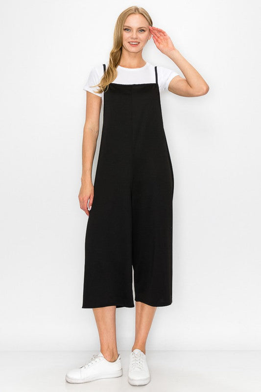 A person models the Stylespect Cropped Bottom Wide Leg Oversized Jumpsuit in black, paired with a white t-shirt and white sneakers, set against a plain white backdrop.