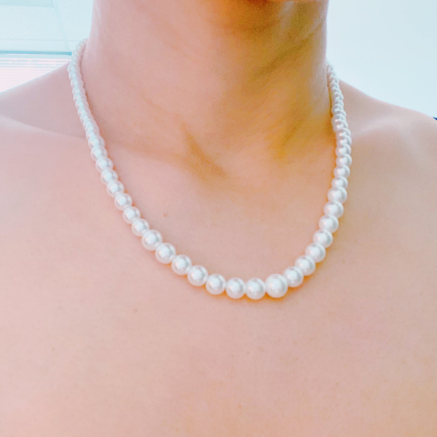 The Queen Liz Graduated Pearl Necklace by Ellison + Young features white pearls with a gold clasp, displayed on a light marble surface.