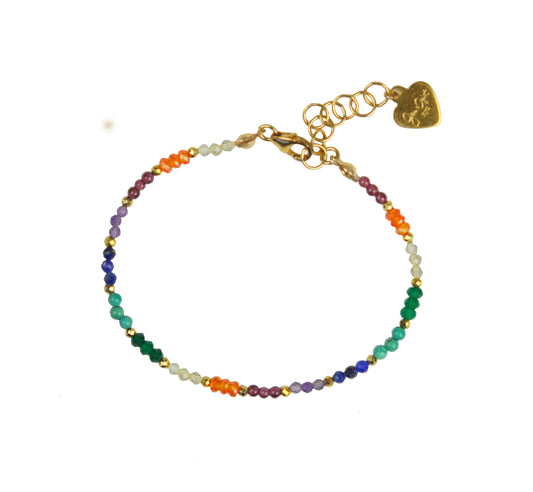 The Chakra Delicate Bracelet by Gena Myint is a colorful, beaded bracelet with a gold chain and a heart-shaped charm, featuring small beads in orange, purple, green, and blue.