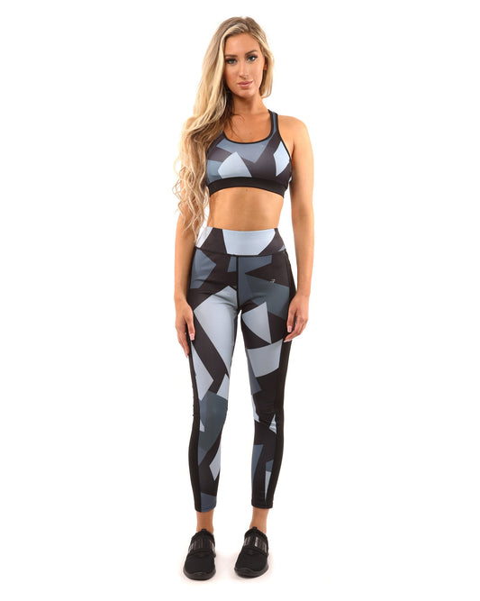 A person wearing the Savoy Active Bondi Set, consisting of geometric-patterned black and grey leggings and a sports bra, stands against a white background.